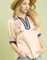 Woman wearing a beige blouse with floral embroidery and a straw hat on a light green background