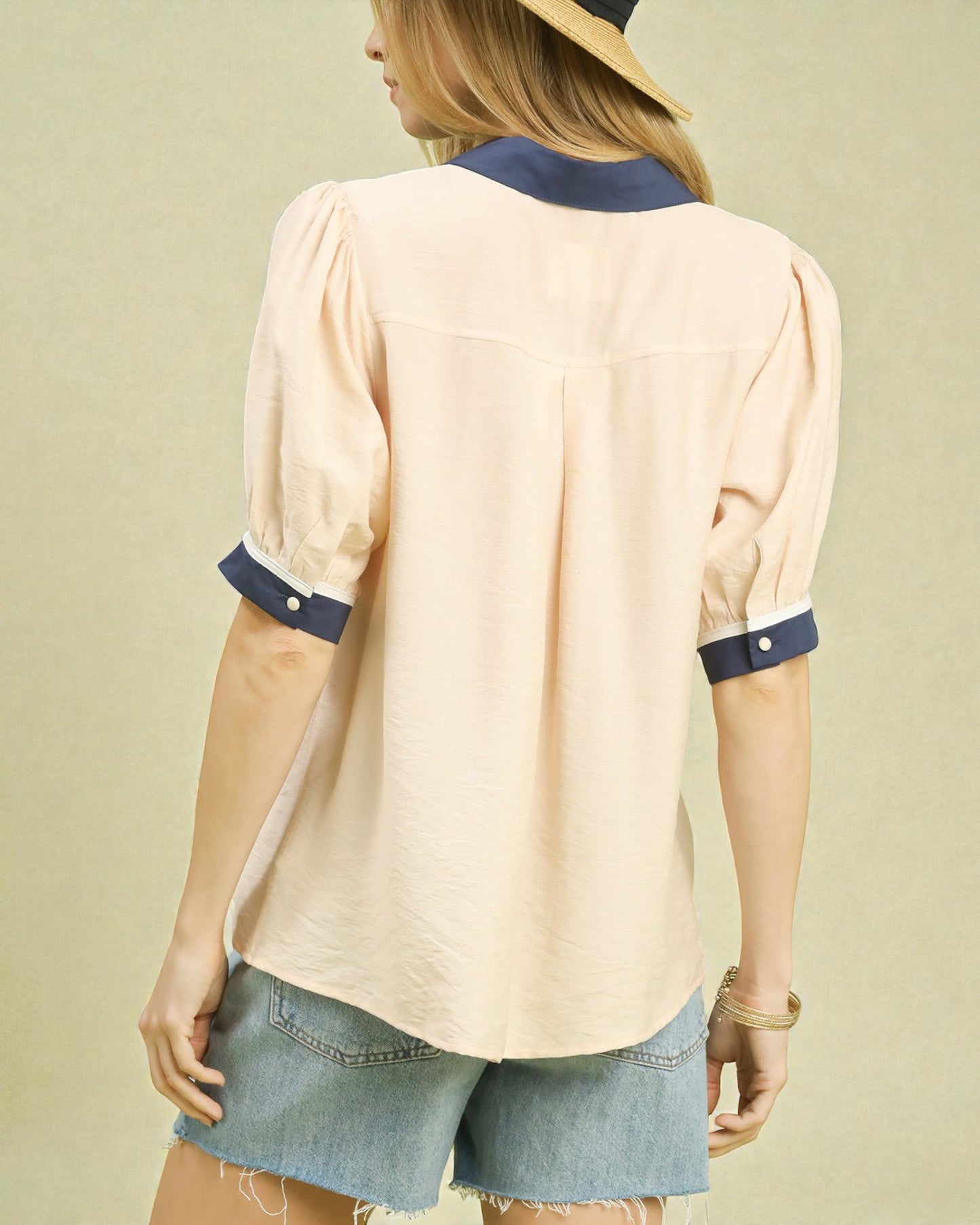 Woman wearing a beige blouse with navy accents and denim shorts on a beige background