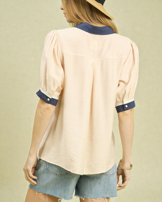 Woman wearing a beige blouse with navy accents and denim shorts on a beige background