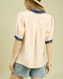 Woman wearing a beige blouse with navy accents and denim shorts on a beige background