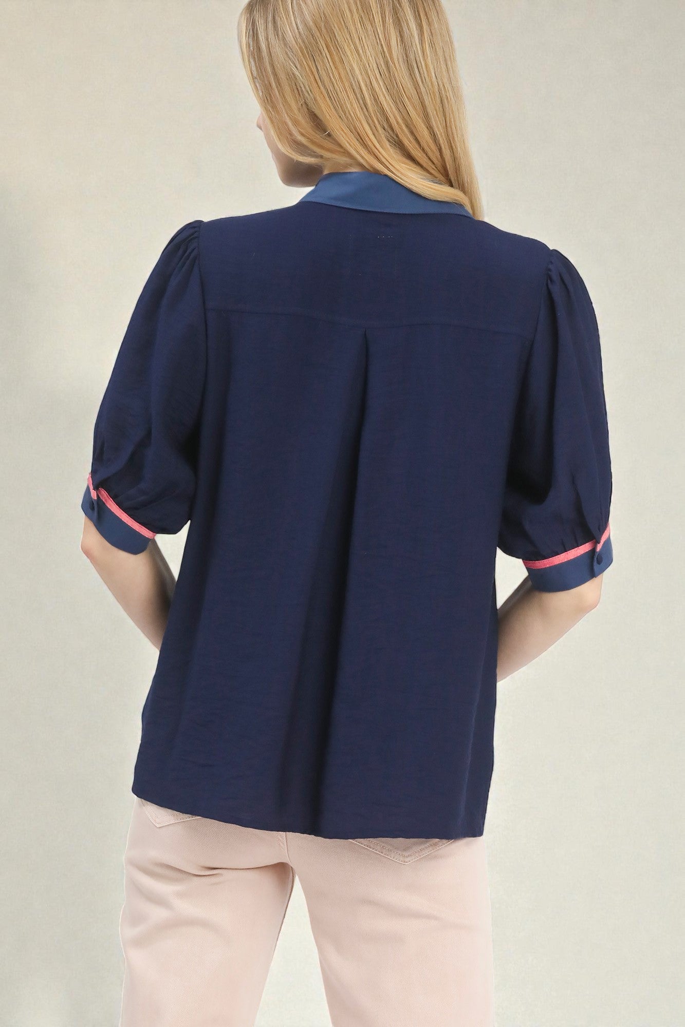 Navy blouse with pink trim worn by a person on a neutral background