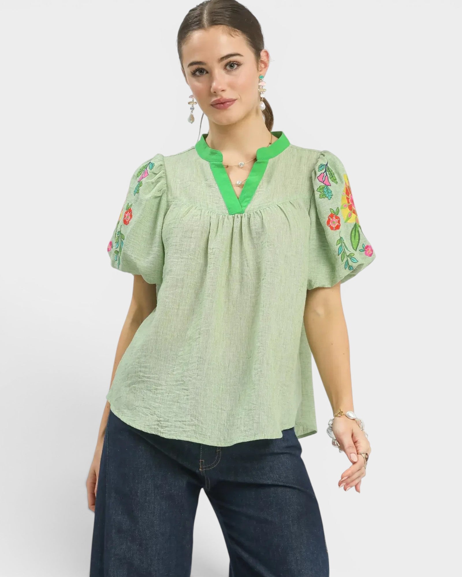 Woman wearing a green blouse with floral embroidery on a white background
