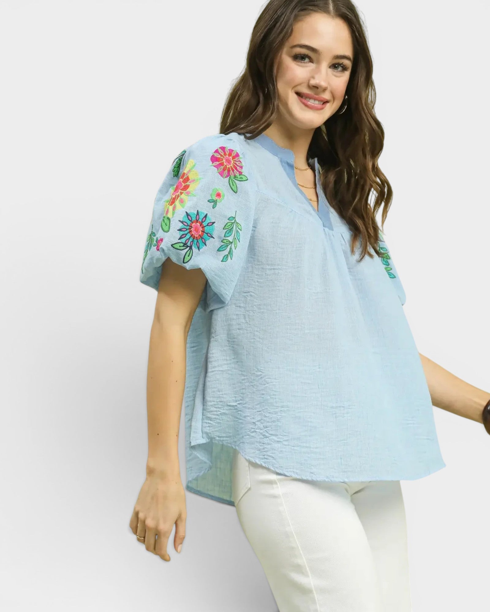 Woman wearing a light blue blouse with floral embroidery on a white background