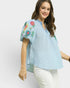 Woman wearing a light blue blouse with floral embroidery on a white background