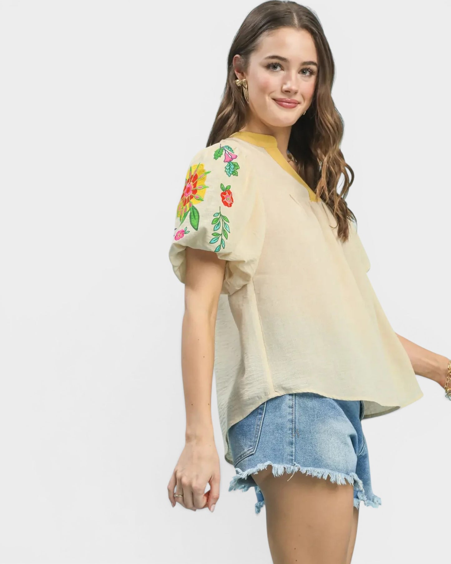 Woman wearing a beige top with floral embroidery and denim shorts on a white background