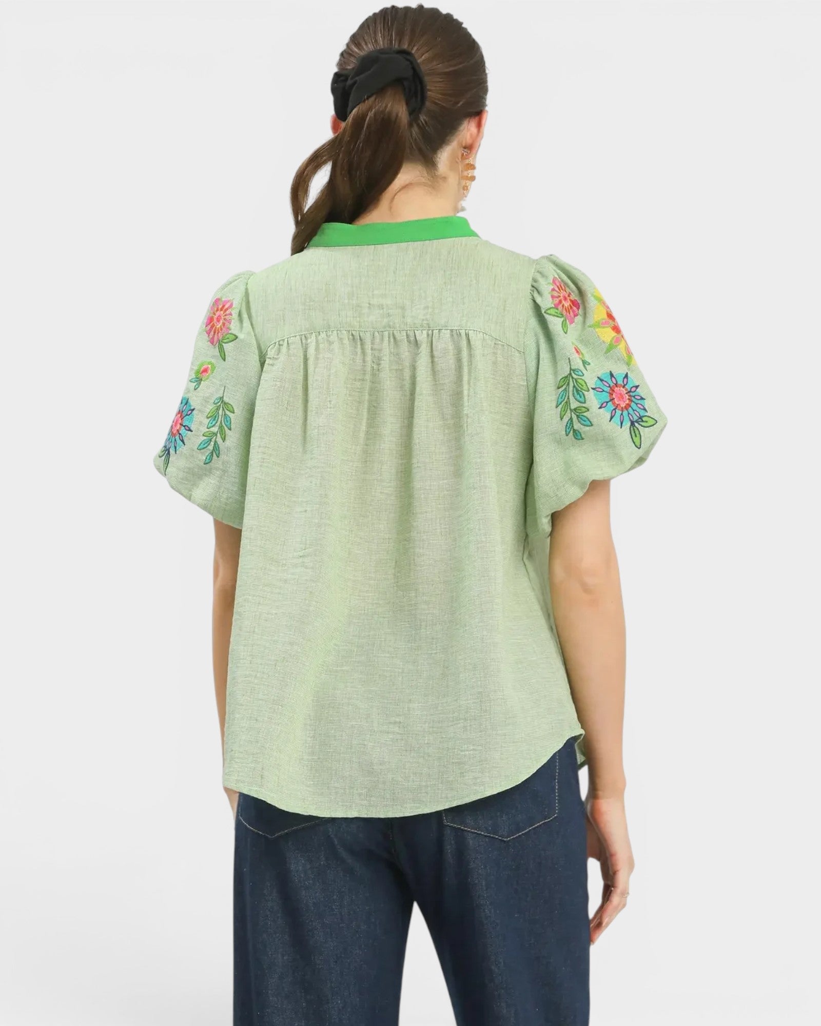 Green blouse with floral embroidery on sleeves worn by a person on a white background