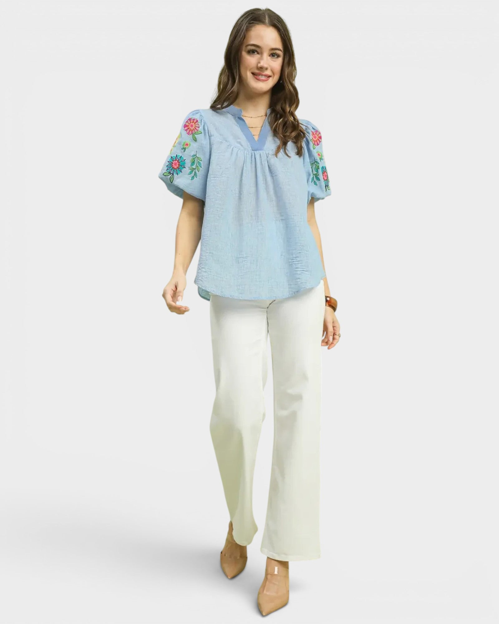 Woman wearing a light blue embroidered blouse and white pants on a white background
