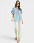 Woman wearing a light blue embroidered blouse and white pants on a white background