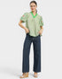 Woman wearing a green blouse with floral embroidery and dark blue jeans on a white background