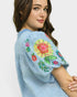 Woman wearing a light blue blouse with colorful floral embroidery on a white background