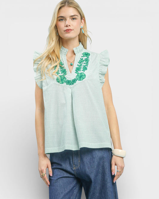 Woman wearing a light green blouse with floral embroidery and blue jeans on a white background