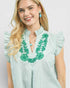 Woman wearing a light green dress with floral embroidery on a plain background