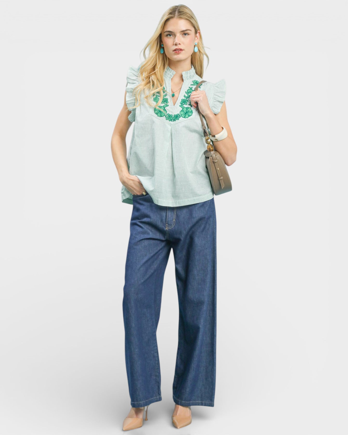 Woman wearing a light blue embroidered blouse and blue jeans on a white background