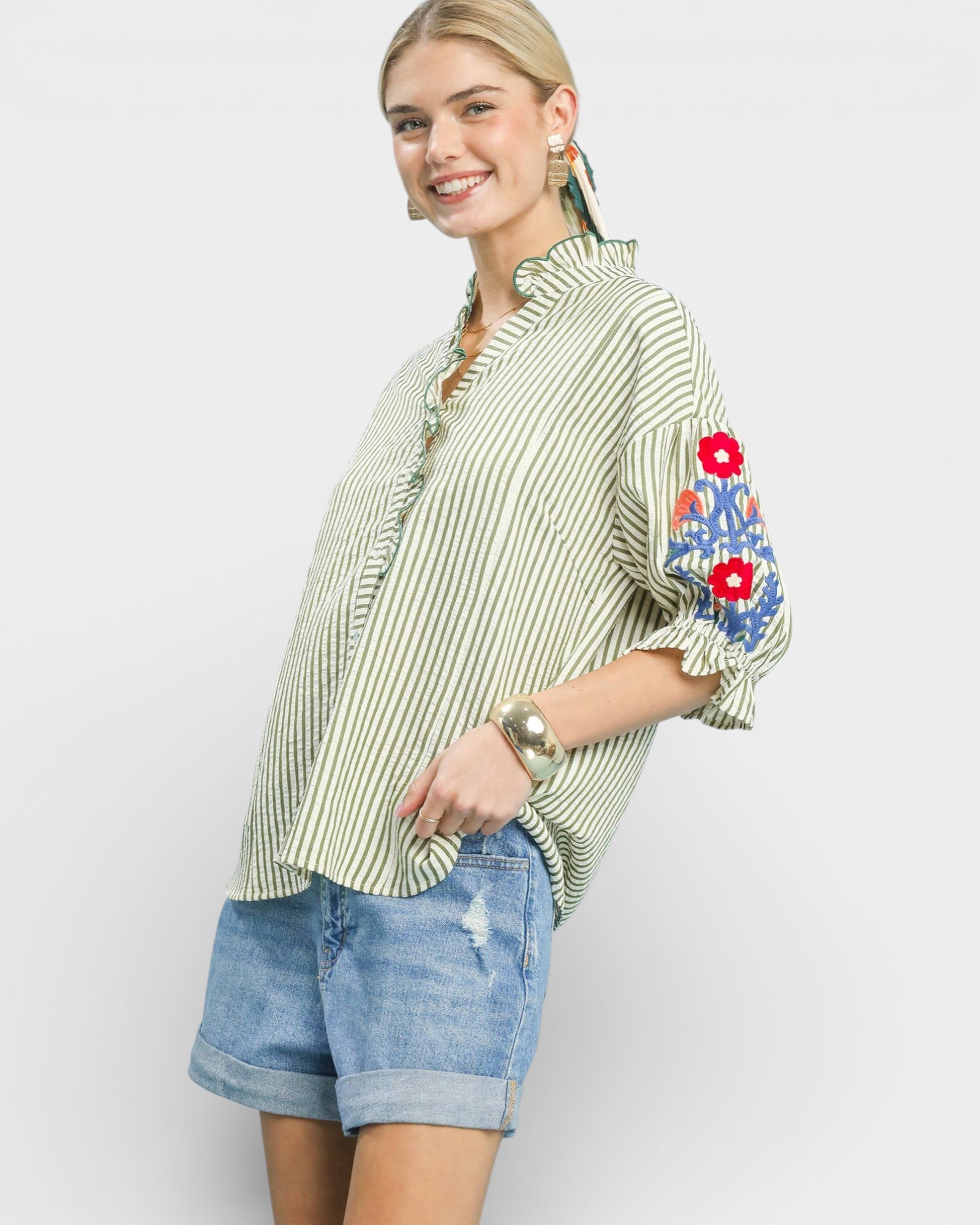 Woman wearing a green and white striped shirt with floral embroidery on a plain background