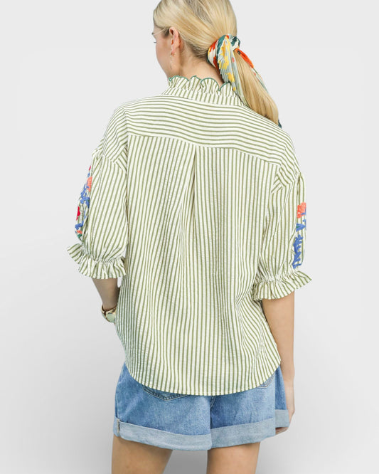 Woman wearing a green and white striped shirt with floral embroidery on a plain background