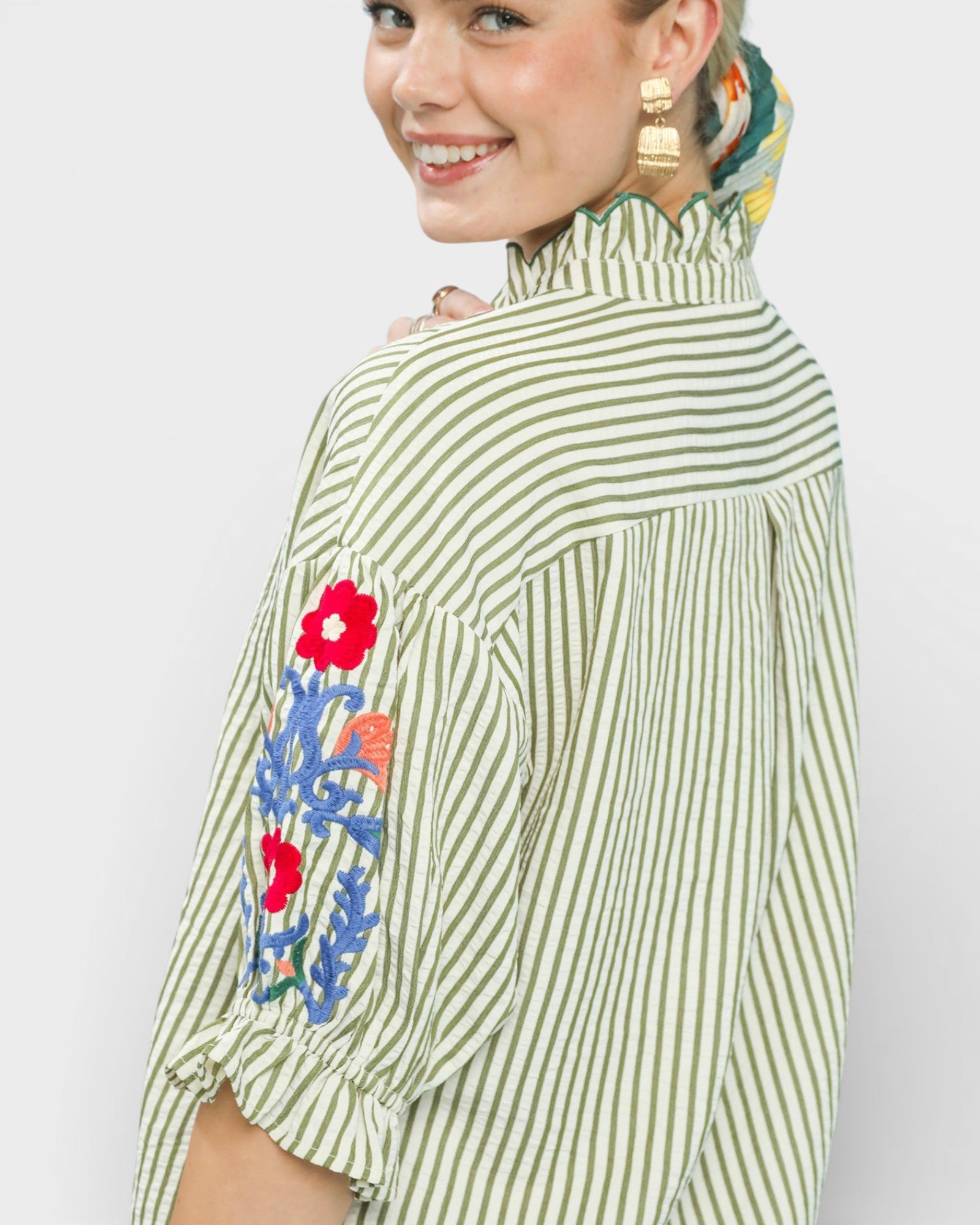 Woman wearing a green and white striped top with floral embroidery on a plain background