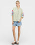 Woman wearing a striped shirt with floral sleeves and denim shorts on a white background