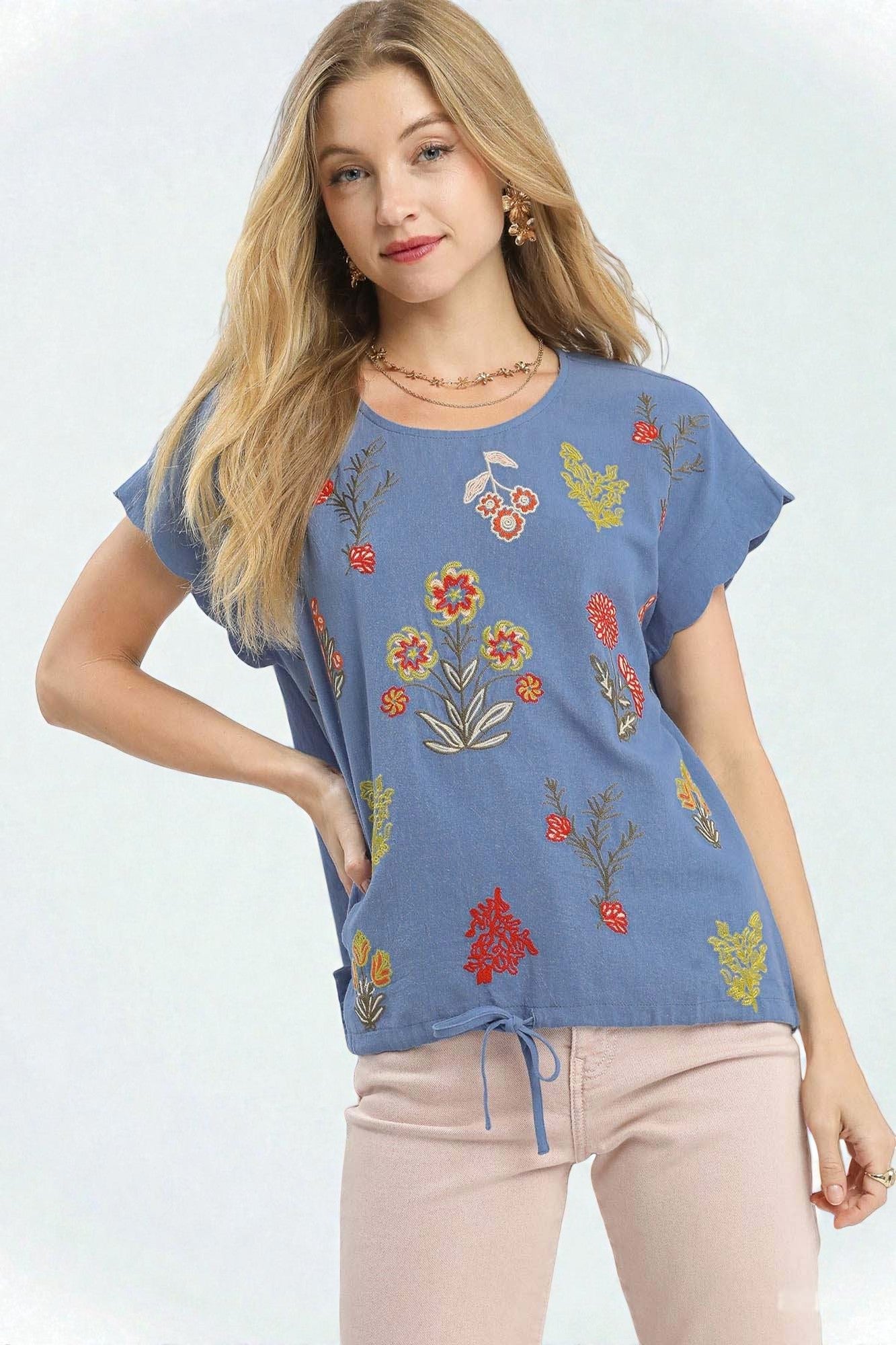 Woman wearing a blue embroidered top with colorful floral designs on a white background