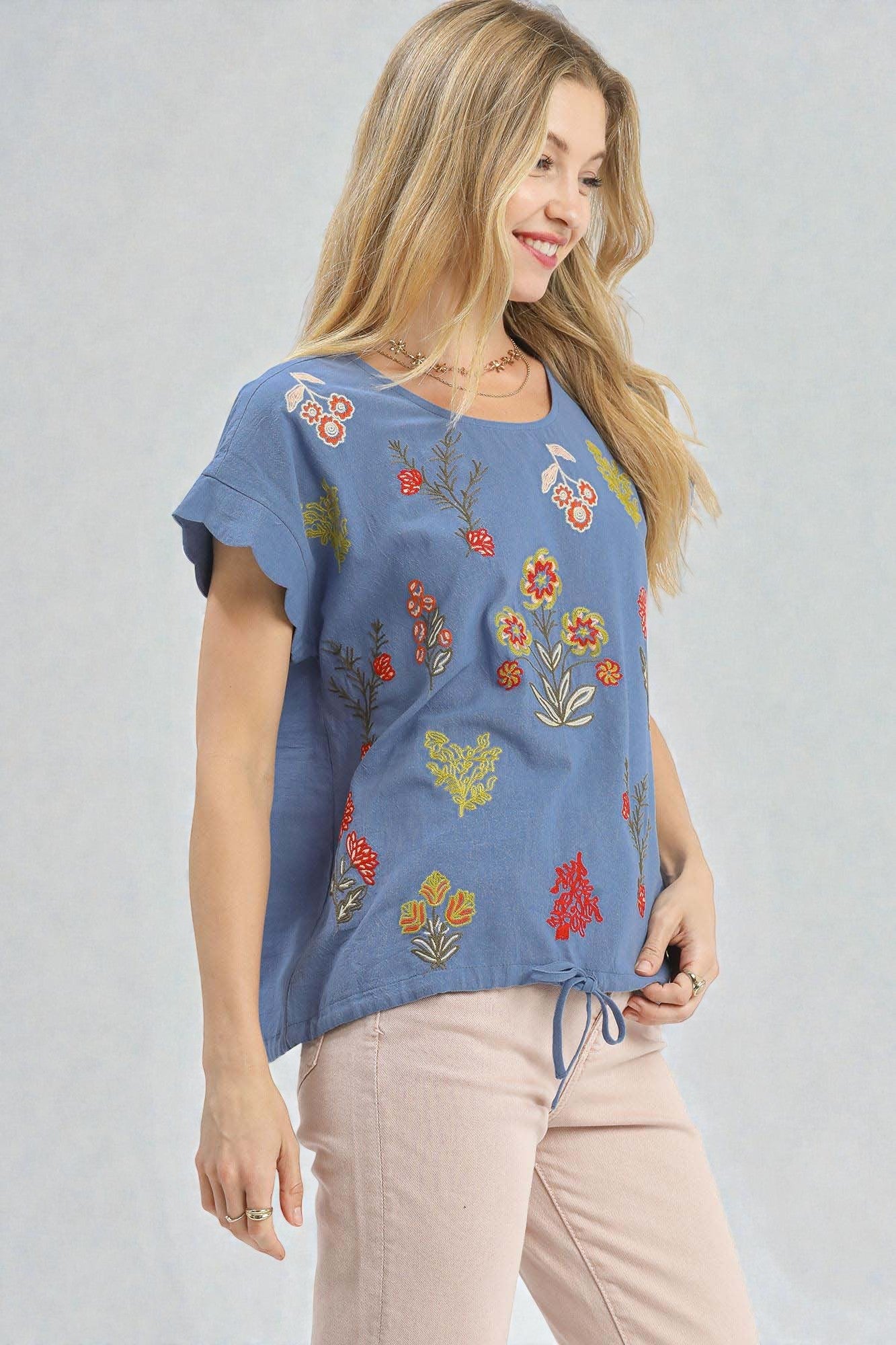 Woman wearing a blue top with floral embroidery on a plain background