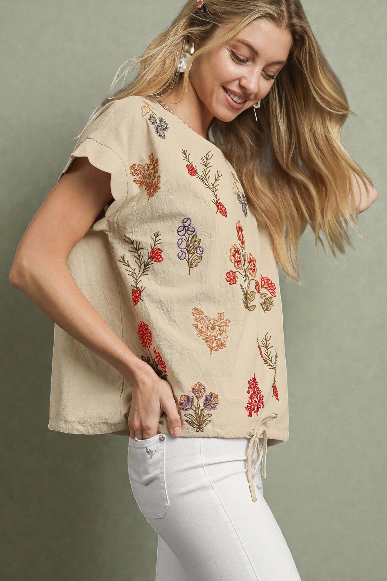 Woman wearing a beige top with floral embroidery against a green background