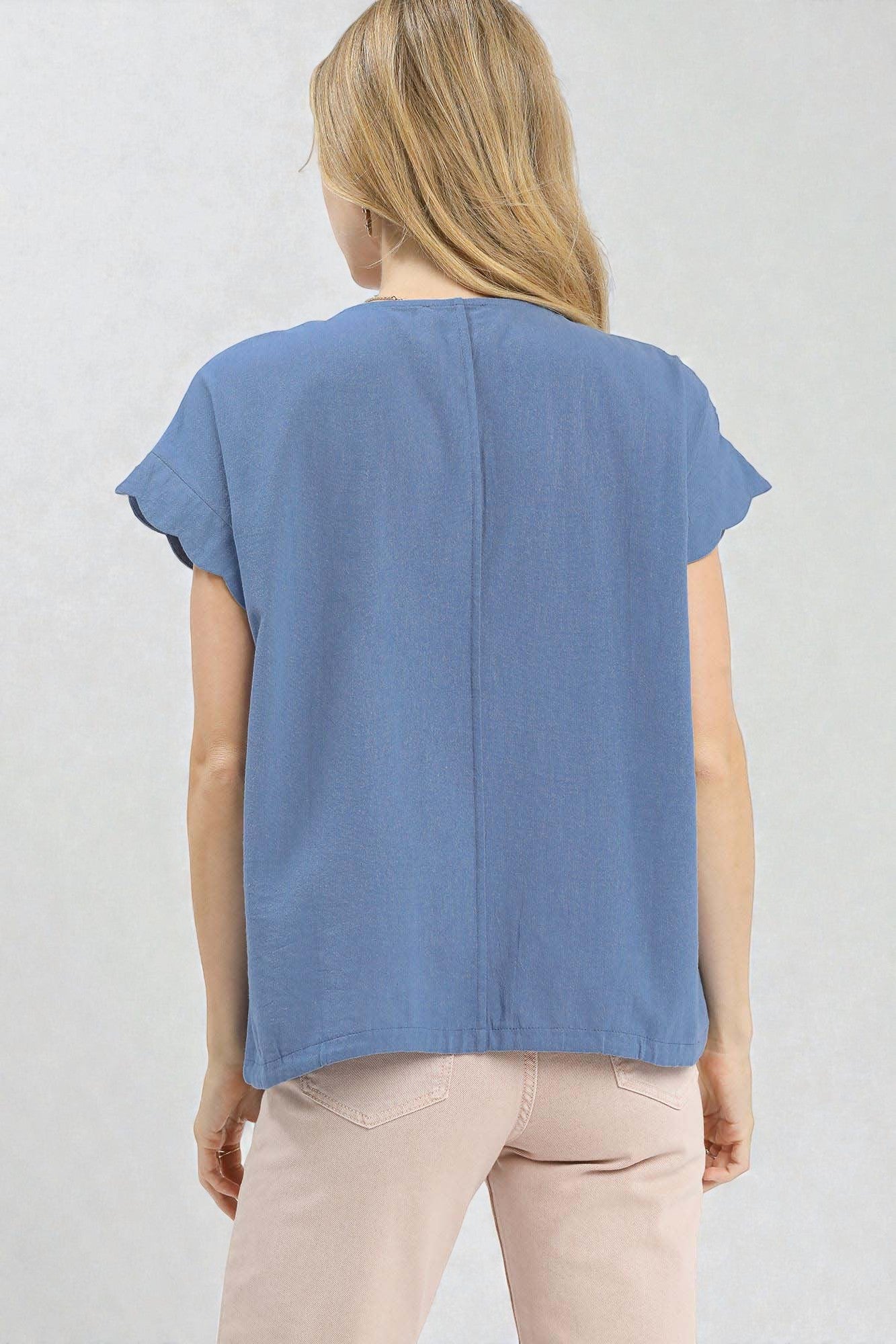 Woman wearing a blue sleeveless top and pink pants against a light gray background