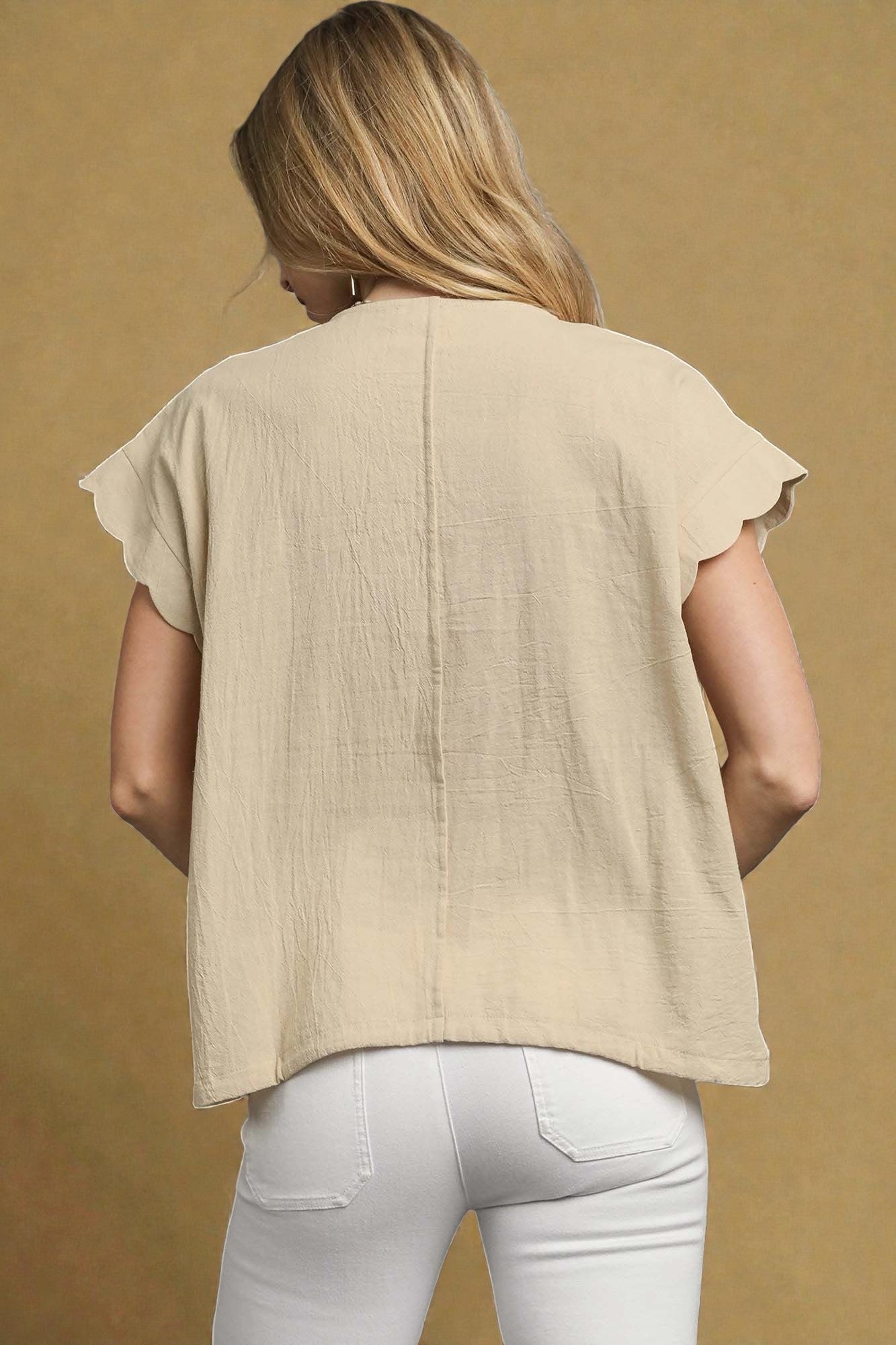 Woman wearing a beige top and white pants against a beige background