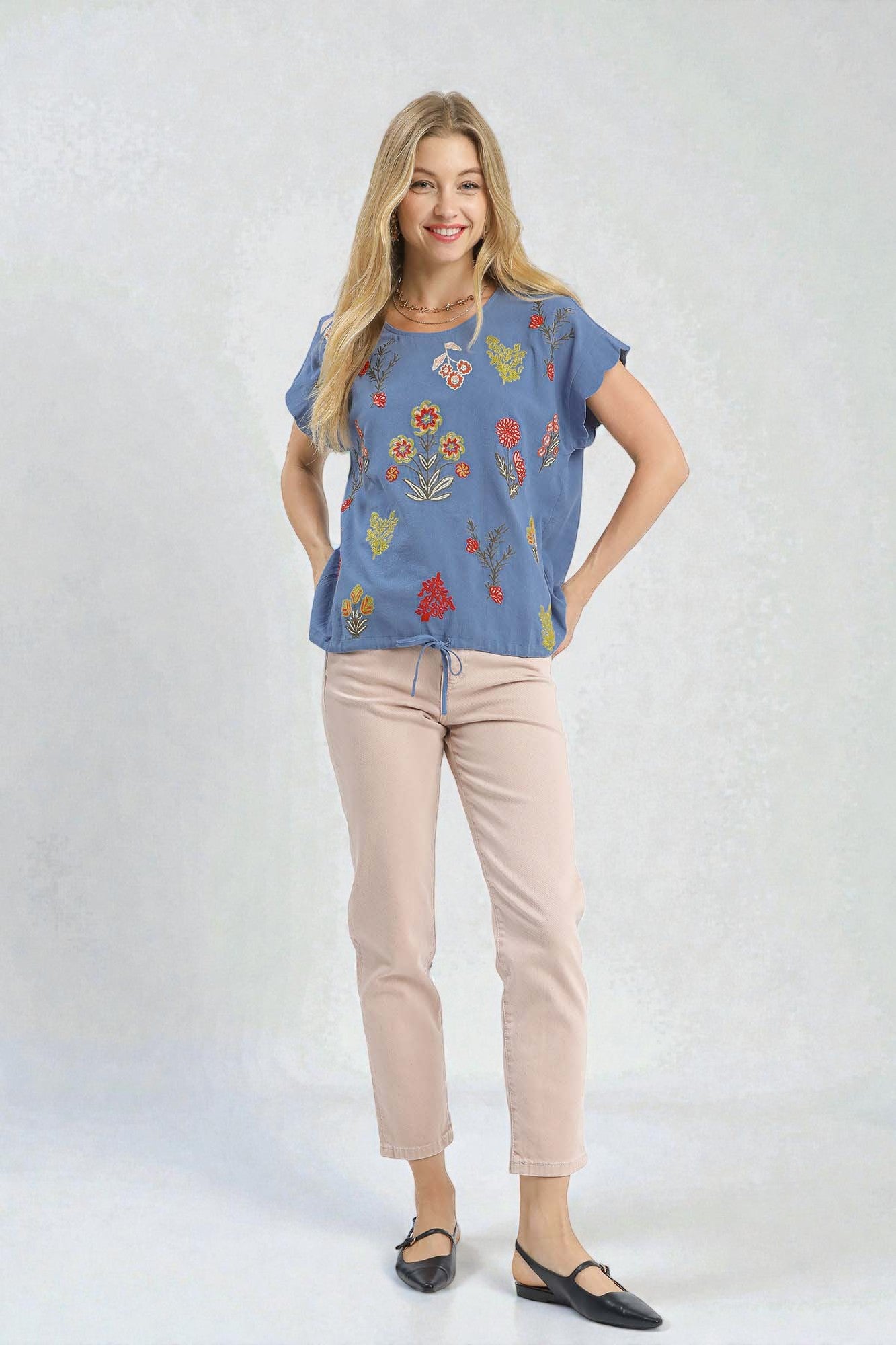 Woman wearing a blue floral top and beige pants on a white background