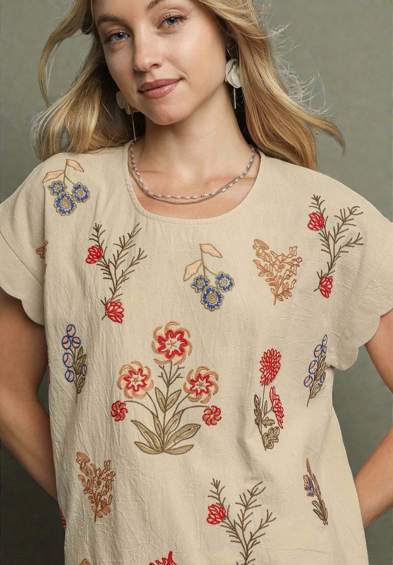 Woman wearing a beige blouse with floral embroidery on a neutral background