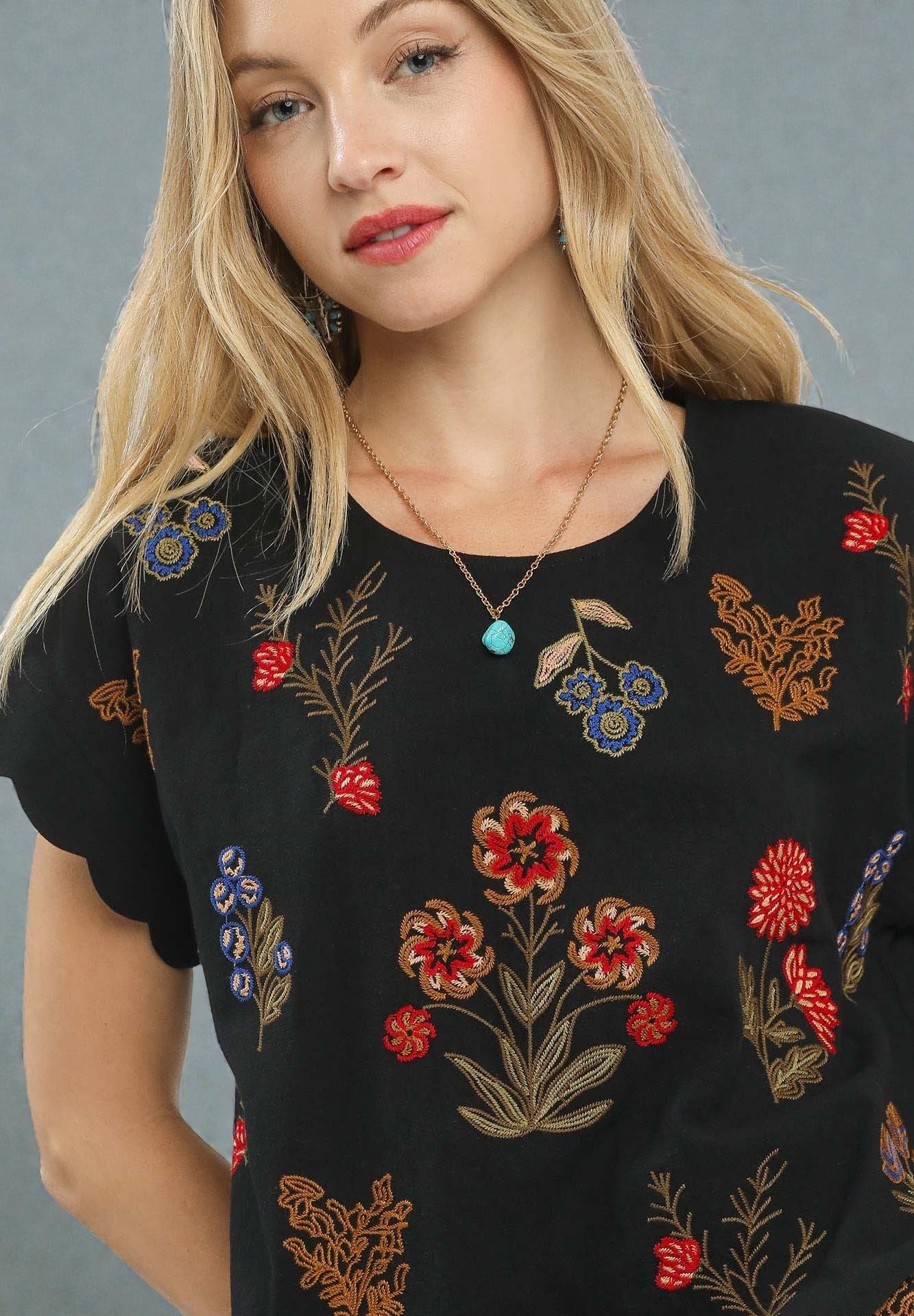 Woman wearing a black top with colorful floral embroidery against a gray background