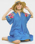 Woman wearing a blue dress with floral embroidery and a straw hat on a white background