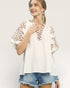 Woman wearing a white blouse with floral embroidery and denim shorts on a light gray background