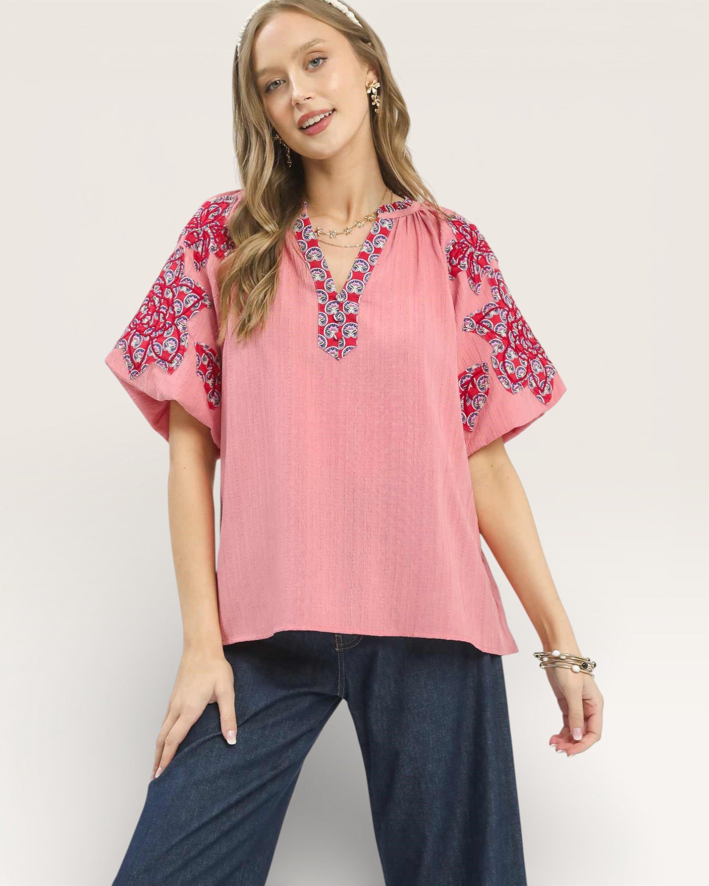 Woman wearing a pink blouse with red floral patterns on a plain background