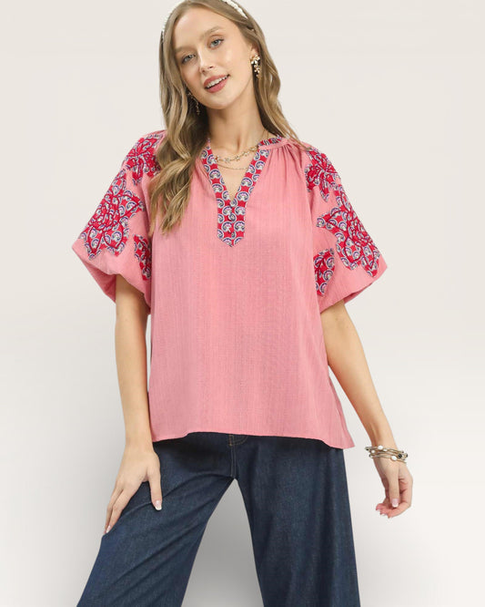 Woman wearing a pink blouse with red floral patterns on a plain background