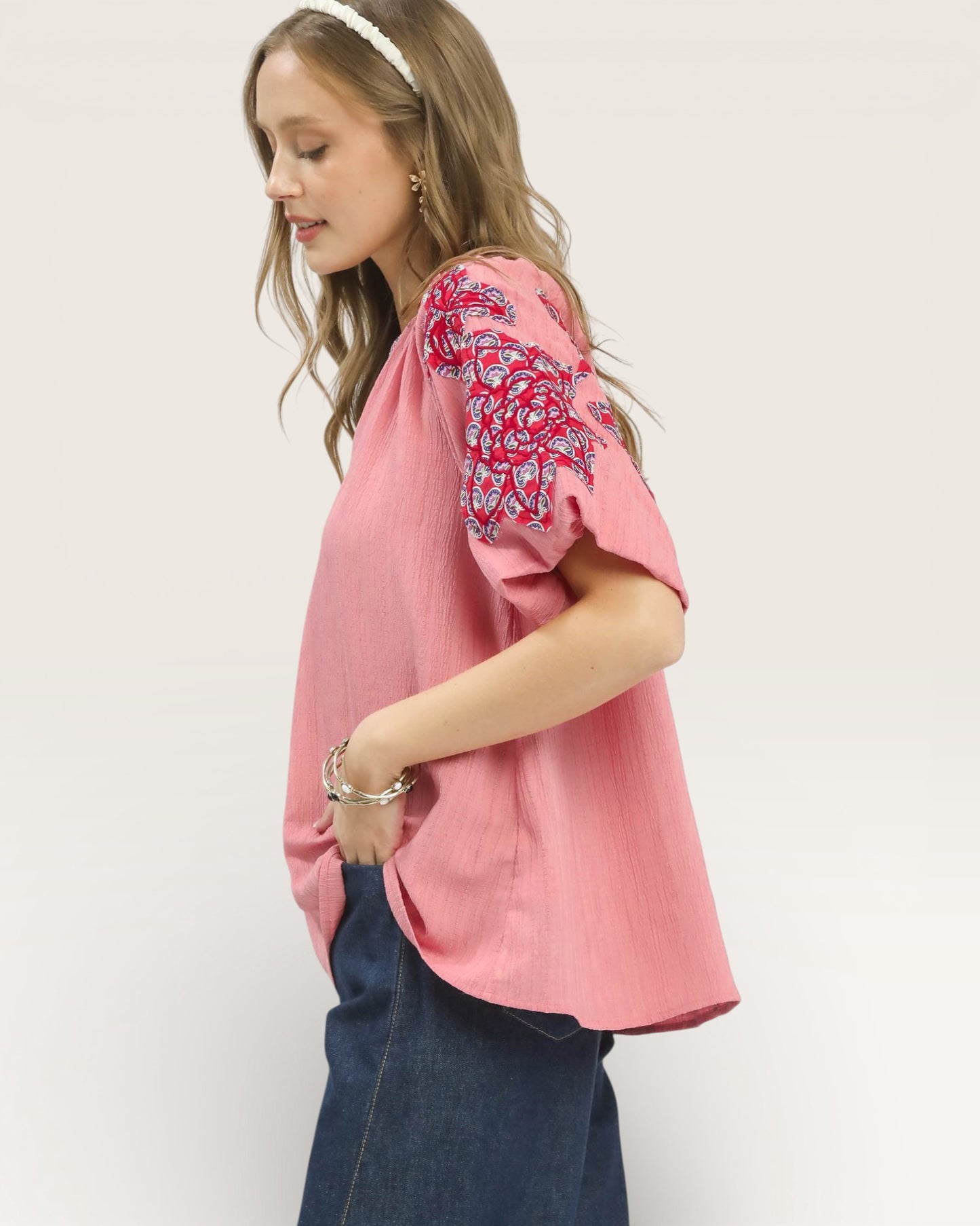 Woman wearing a pink blouse with floral embroidery on a white background