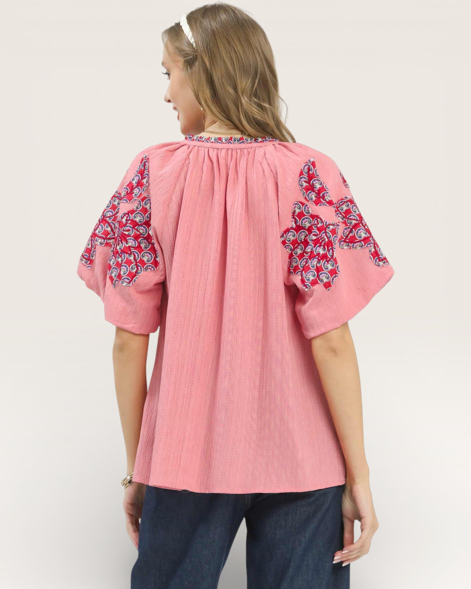 Woman wearing a pink blouse with floral sleeves on a plain background