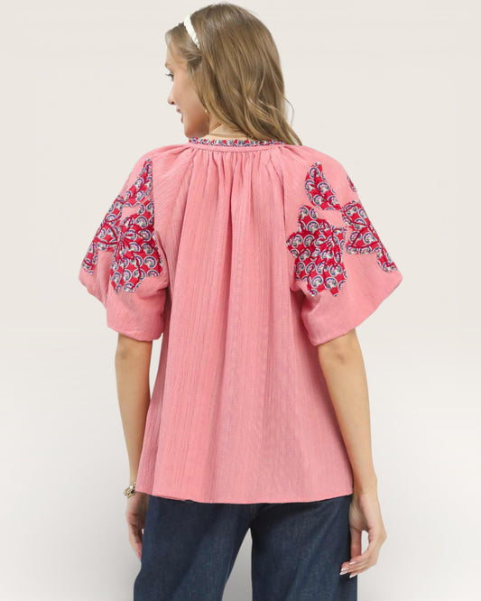 Woman wearing a pink blouse with floral sleeves on a plain background