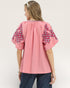 Woman wearing a pink blouse with floral sleeves on a plain background