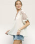 Woman wearing a white blouse with floral sleeves and denim shorts on a plain background