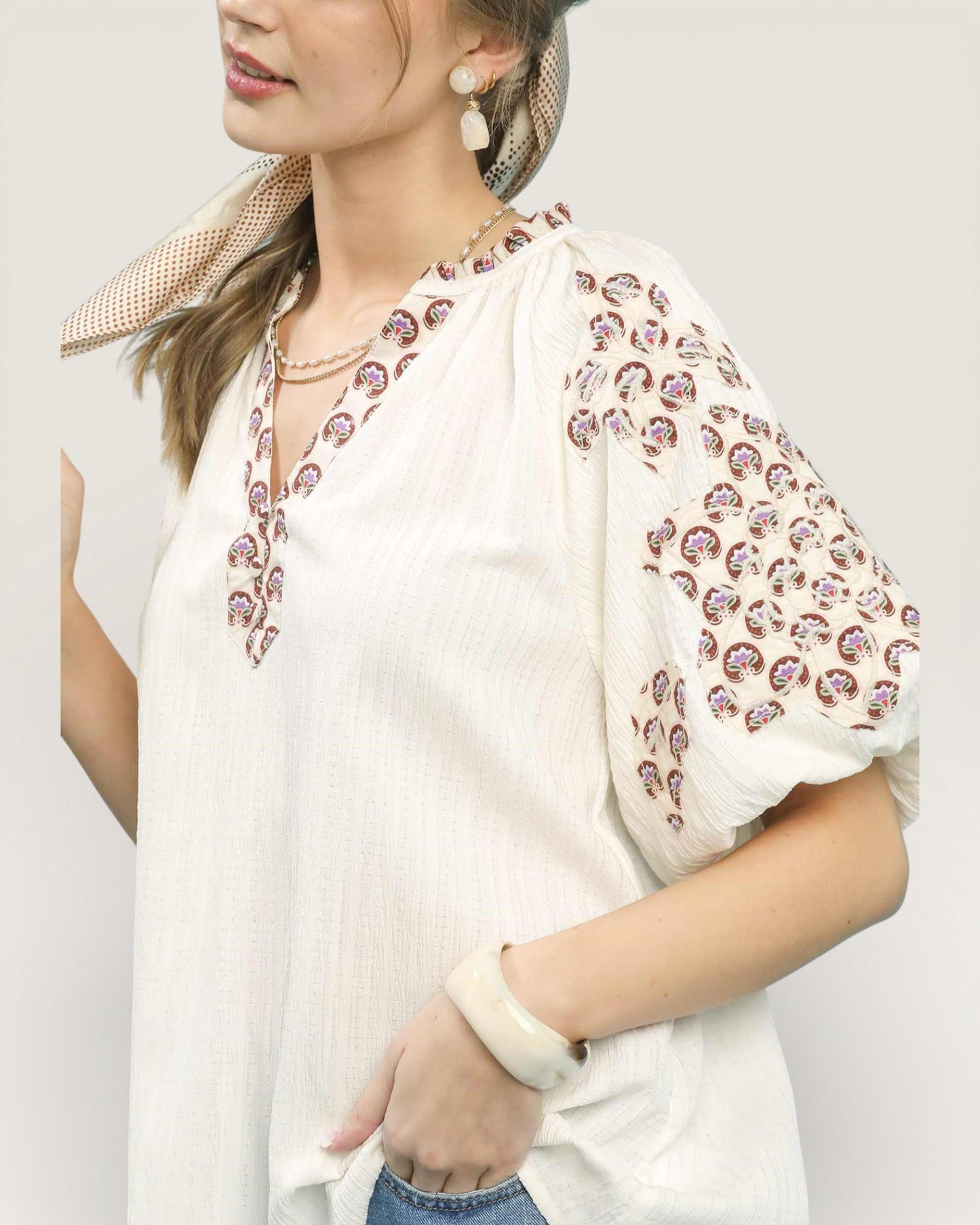 Woman wearing a white blouse with floral patterns on a plain background