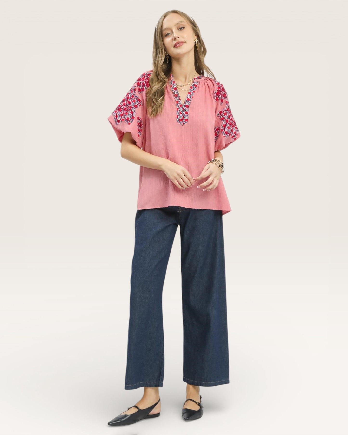 Woman wearing a pink blouse with floral embroidery and blue jeans on a white background