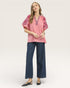 Woman wearing a pink blouse with floral embroidery and blue jeans on a white background