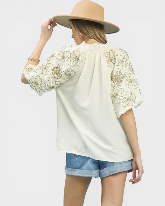 Woman wearing a cream blouse with floral embroidery and denim shorts on a white background