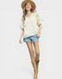 Woman wearing a cream blouse with lace sleeves, denim shorts, and tan cowboy boots on a white background