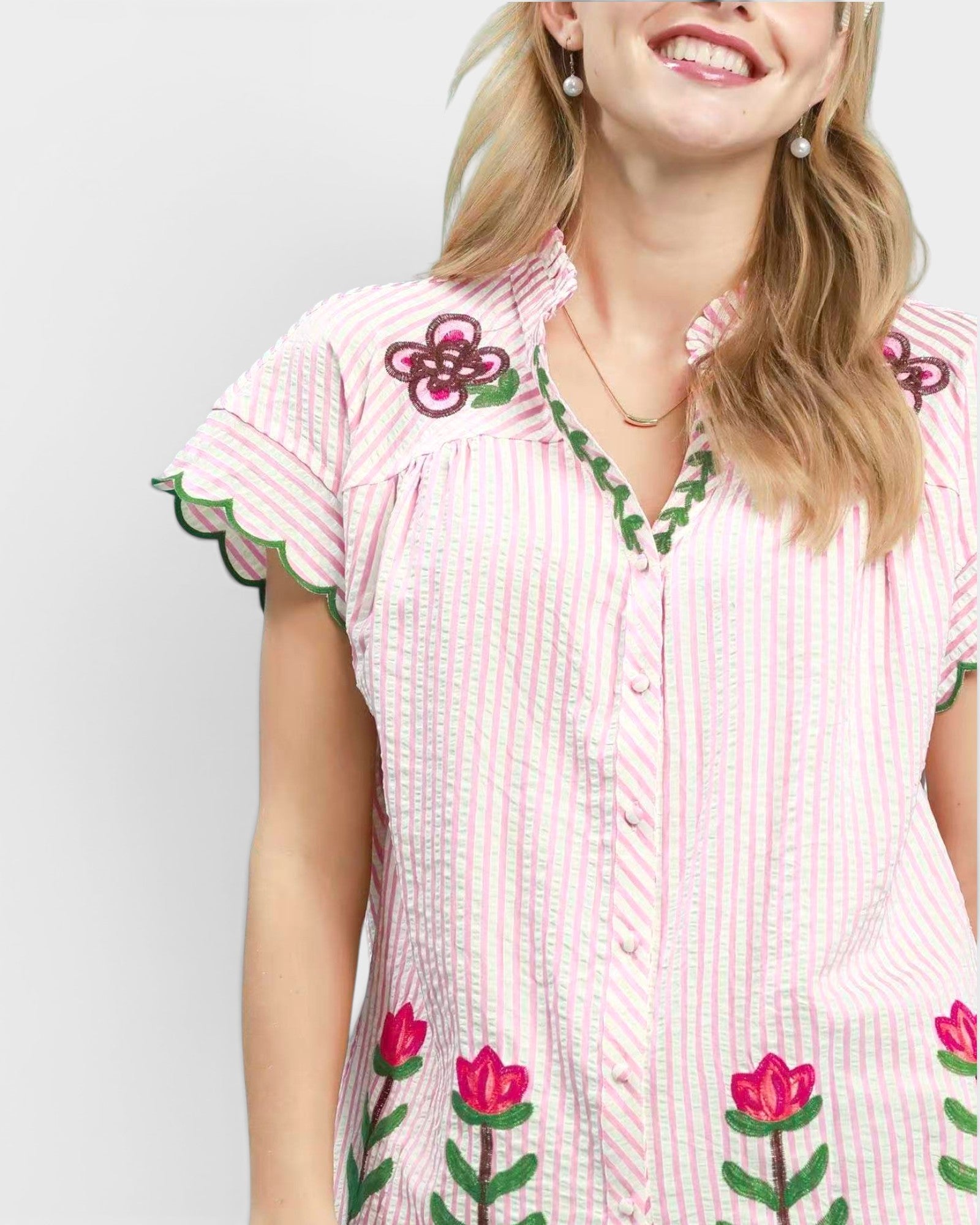 Woman wearing a pink and white dress with floral embroidery on a plain background