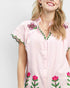 Woman wearing a pink and white dress with floral embroidery on a plain background