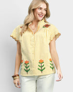 Woman wearing a yellow striped shirt with floral designs on a plain background