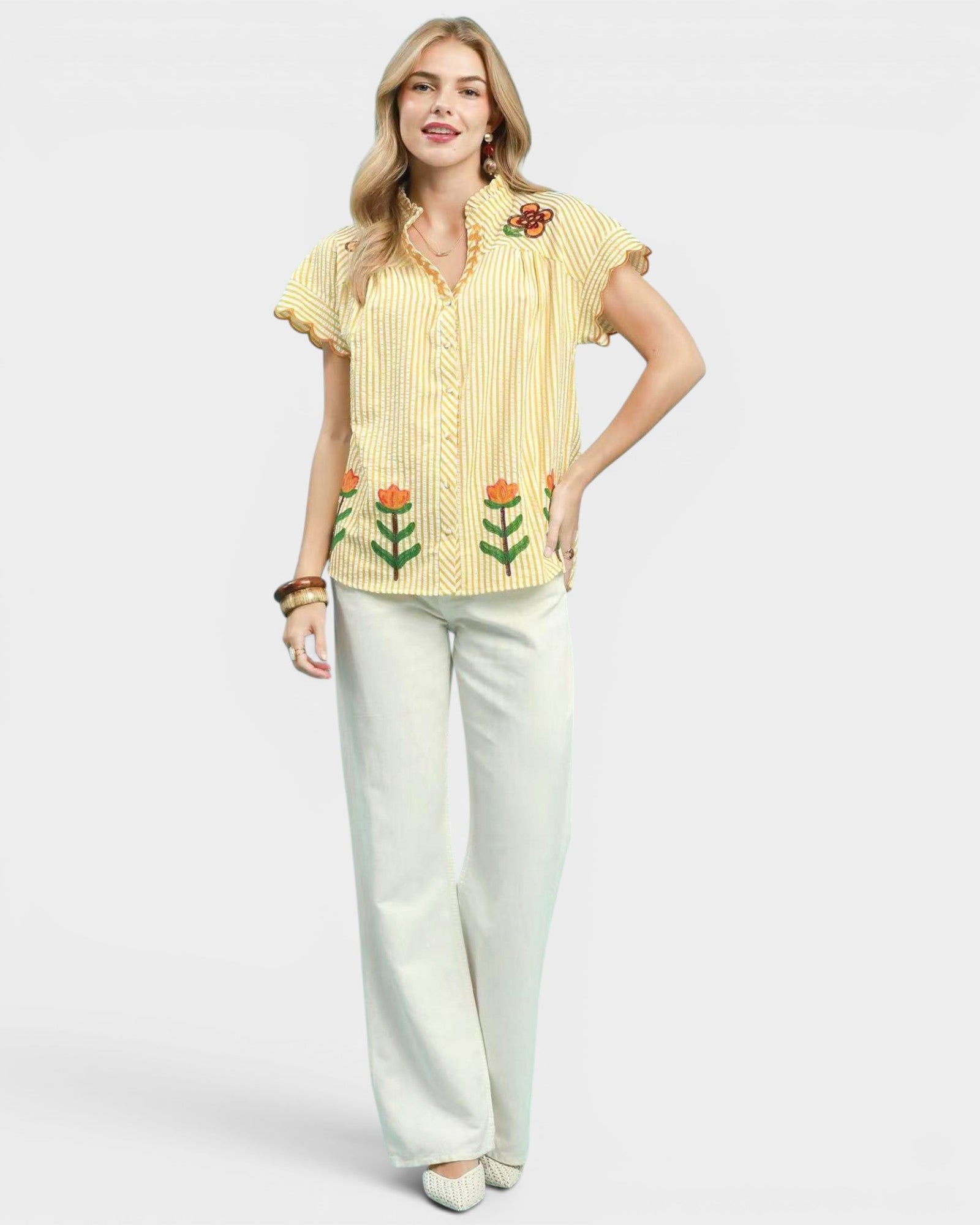 Woman wearing a yellow embroidered blouse and white pants on a white background