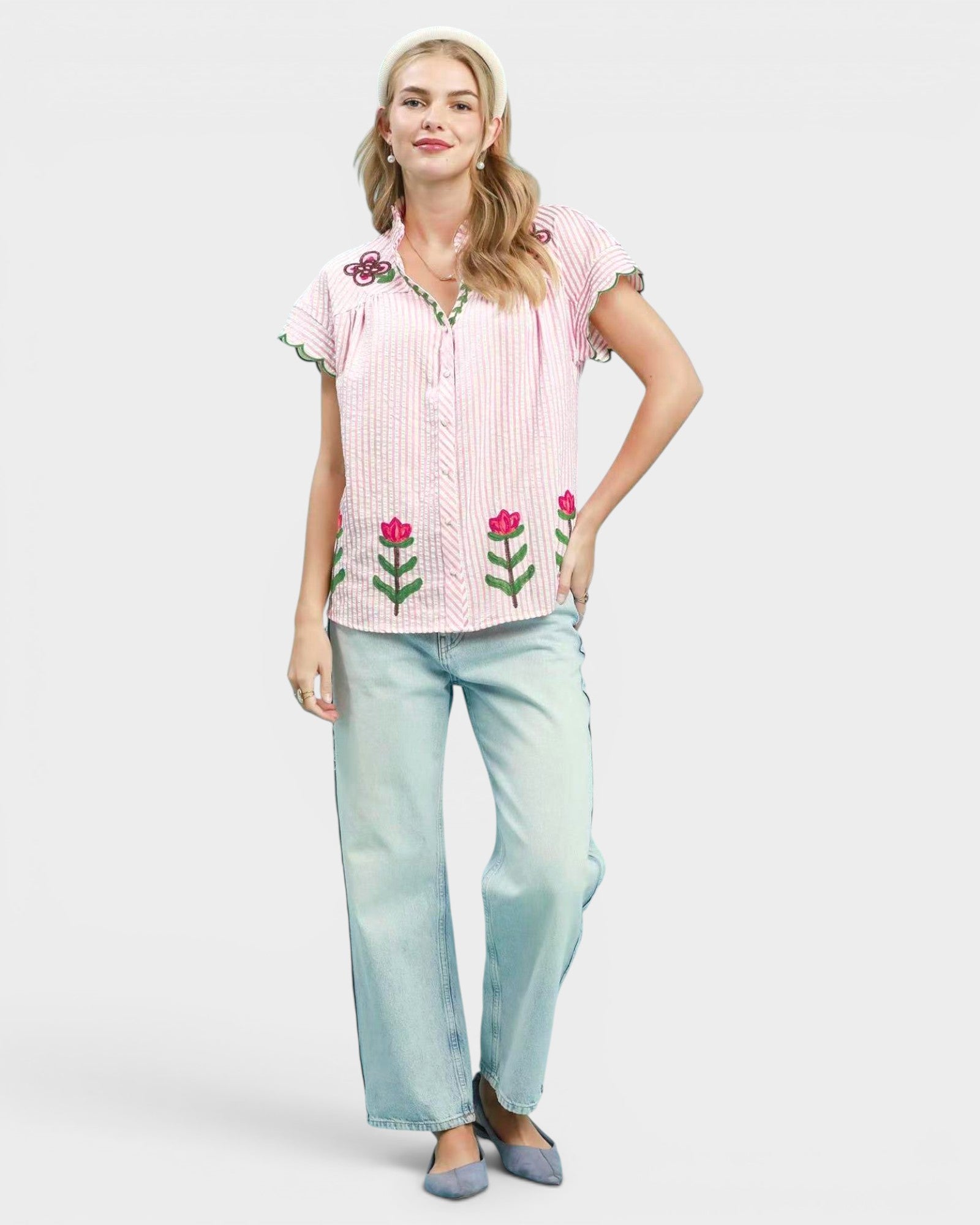 Woman wearing a pink embroidered shirt and light blue jeans on a white background