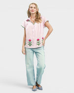 Woman wearing a pink embroidered shirt and light blue jeans on a white background