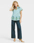 Woman wearing a blue and white striped shirt with floral embroidery and dark jeans on a white background
